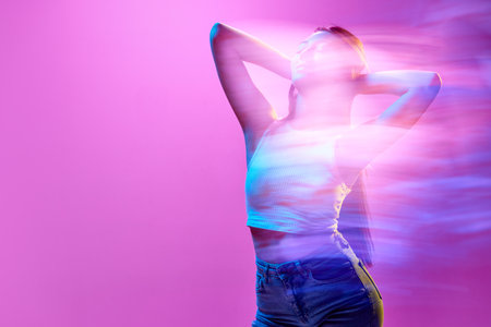Portrait of young elegant woman posing against light purple background in neon lights. Silhouette. Lights reflectionの写真素材
