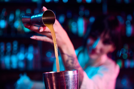 Young beautiful woman, bartender making cocktails, working in bar, pouring liquid from jigger into...