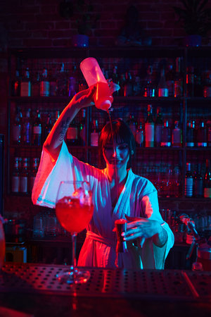 Pretty young girl, professional bartender making delicious cocktails, pouring liquid into jigger, measuring amount of syrupの写真素材