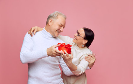 Happy, caring, loving senior couple, man and woman celebrating holiday, presenting gifts against pink studio background. Valentines Dayの写真素材