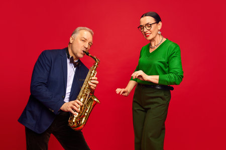 Caring, loving man, husbands playing saxophone to his beautiful wife against red studio background. Romantic date, holiday. Valentines Dayの写真素材