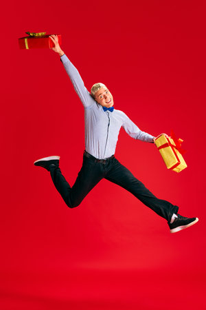 Happy and excited young man emotionally jumping with present boxes against red studio background. Christmas, winter holidaysの写真素材