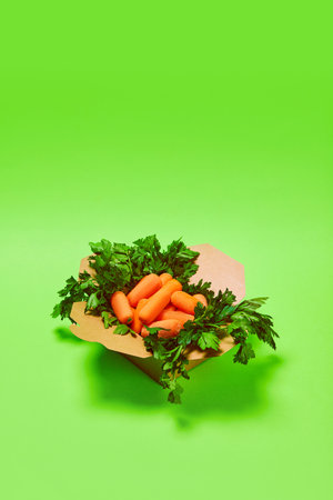 Healthy snack in carton box. Fresh washed carrots against green background. Organic products and healthy foodの写真素材