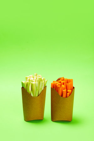 Cut, fresh celery and carrot placed into carton packaging for fries against green background. Healthy snacks. Organic products and healthy foodの写真素材