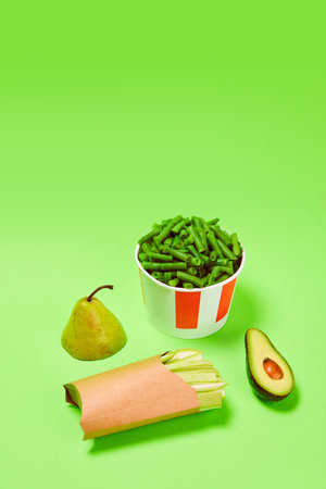 Healthy snacks. Green beans into popcorn basket, avocado, celery and pear against green background....