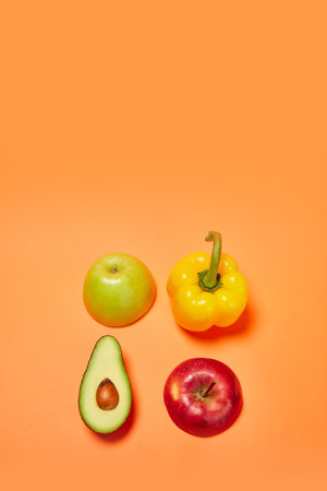 Yellow sweet pepper, green and red apple, avocado against orange background. Flat lay. Organic products and healthy foodの写真素材