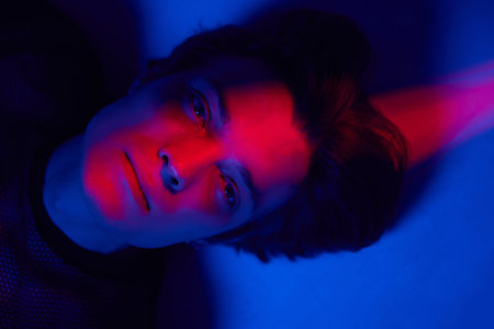 Portrait of handsome young man, male model lying on floor and posing against dark blue background...