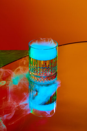 Glass with strong drink, whiskey and smoke on top standing against orange background in neon light