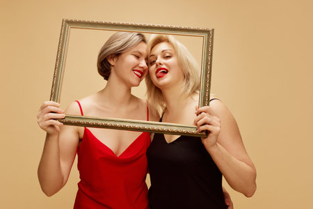 Happy beautiful women, lesbian women standing in dresses, posing with picture frame over light...