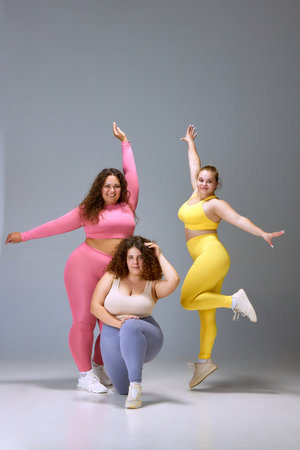 Happy, smiling, positive three young women with oversized bodies, standing in colorful sportswear...