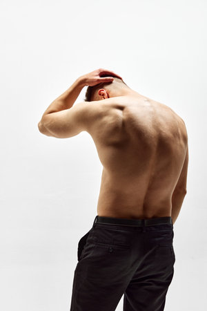 Round back. Shirtless young man with muscular relief body standing in pants isolated over white...