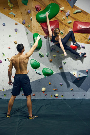 Muscular shirtless young man, bouldering training teaching young girl to climb wall. Sportive meetingの写真素材