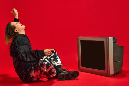 Young man raising hand of happy and joy because he winning level in video game which he play on retro TV set against red background.の写真素材