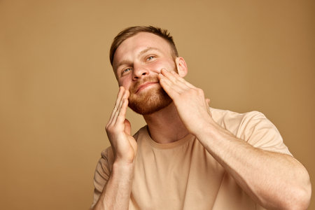 Close up portrait of young attractive man enjoyed effect after using beauty product, moisturized cream for facial care against beige background.の写真素材