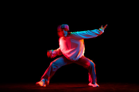 Young woman in casual clothes dancing hip hop isolated over black background in neon light with mixed lights effectの写真素材