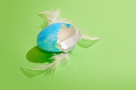 Cracked painted egg with paper and feather inside over green background. Whishes. Easter holiday