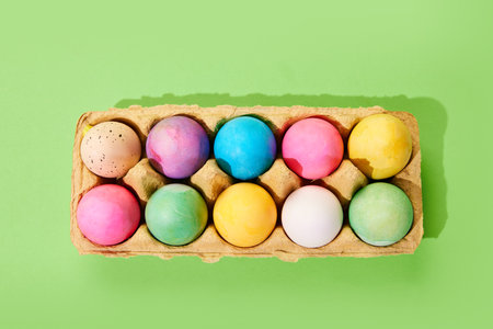 Multicolored painted Easter eggs on carton egg box isolated green background. Top view. Ester,...