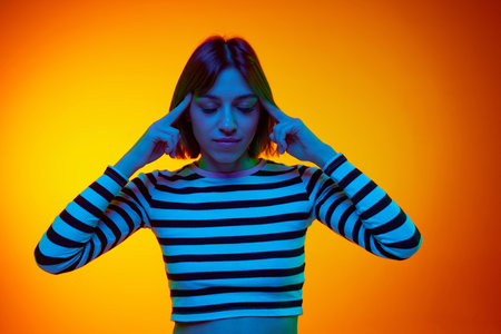 Brainstorming. Portrait of she put her hands to head and closed eyes, concentrating on her thoughts against gradient orange background.の写真素材