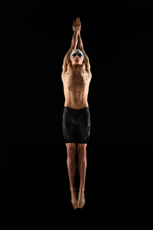 Full-length image of muscular young man, professional swimmer with muscular relief body shape training, showing swimming techniques over black backgroundの写真素材