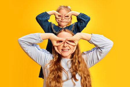 Joyful moments of life. Happy smiling young mother and daughter showing fun and joy against yellow studio background. Mothers Day, International Happiness Dayの写真素材