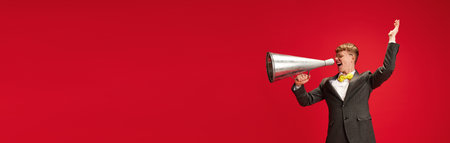 Announcement. Yong man in formalwear talking in megaphones against red studio backgroundの写真素材