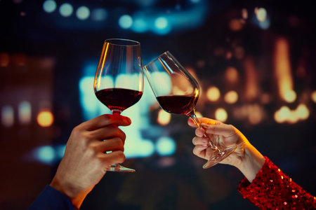 Anniversary celebration, Valentines day date. Male and female hands clinking glasses with red wine over restaurant backgroundの写真素材