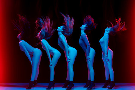 Impressive performance. Young women in bodysuits dancing on high heels against black background in neon lightの写真素材