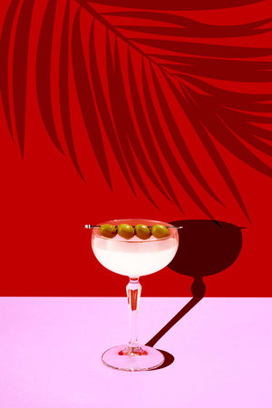 Contemporary art collage. Refreshing sweet and sour Margarita cocktail stands on pink bar counter against red background with shadows of tropical plants.の写真素材