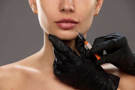Lip augmentation. Cropped image of female face, woman doing lip injections in clinic against studio backgroundの写真素材