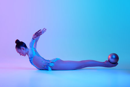 Artistic teen dancer, rhythmic gymnast performing with ball against gradient studio background in neon lightの写真素材