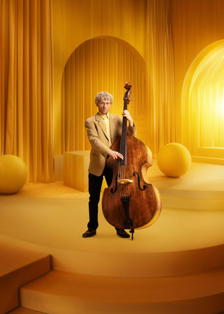Male musician in suit with double bass in monochromatic yellow luxurious room. Elegance and classical tasteの写真素材