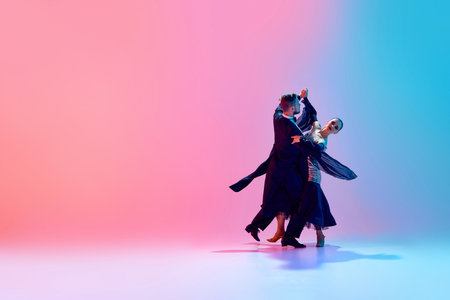 Young man and woman, talented ballroom dancers in motion, dancing in black costumes against gradient pink blue background in neon lightの写真素材
