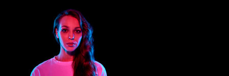 Portrait of beautiful young woman with brunette curly hair looking at camera against black studio background in neon lightの写真素材
