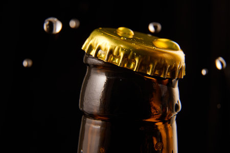 Close-up of opening glass beer bottle with golden cap with water droplets, condensation against...