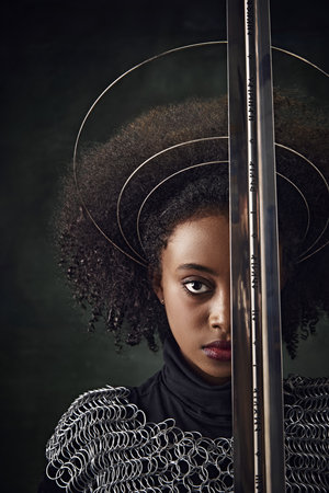 Half-face portrait of African woman with circular halos around her head and chainmail attire holding...