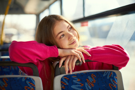 Young girl in pink hoodie sitting in public transport, modern tram, bus, leaning on sits and...