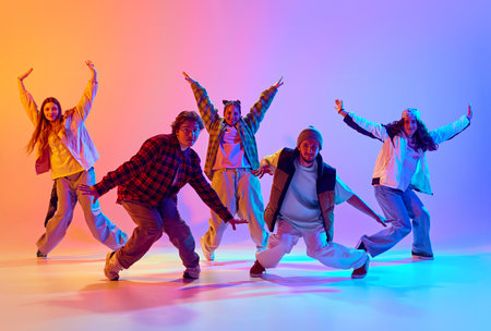 Dynamic image of young people, men and women in casual clothes dancing contemp against gradient studio background in neon lightの写真素材