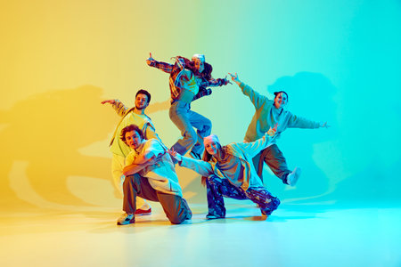 Diverse people, dancers in colorful casual clothes, standing in dynamic jumping pose, performing against gradient green yellow background in neon light.の写真素材