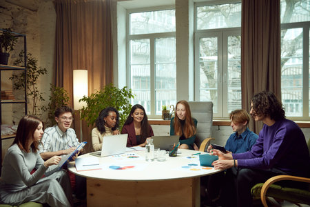 Group of young people sitting at the table, student studying with laptops and papers together on...