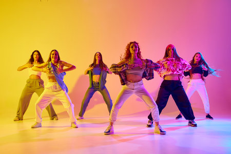 Artistic, talented young women in motion, dancing street style dance against gradient background in neon lightの写真素材