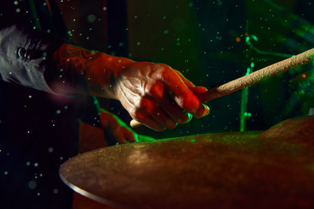 Focus on male hand, musician playing drums over black background with colorful lights and water drops. Poster for a live concertの写真素材