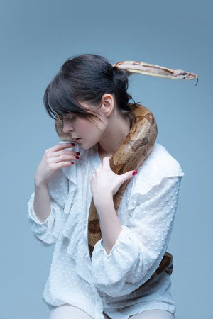 Inner-self and psychology. Portrait of beautiful brunette woman in white blouse posing with snake...
