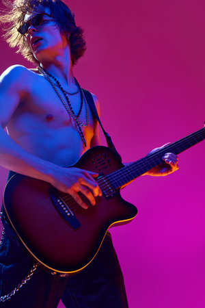 Talented and artistic young man, shirtless musician playing electric guitar against pink background in neon lightの写真素材