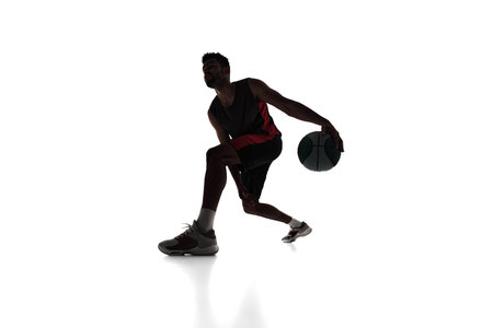Silhouette of concentrated male athlete, basketball player in motion, dribbling ball isolated on white backgroundの写真素材