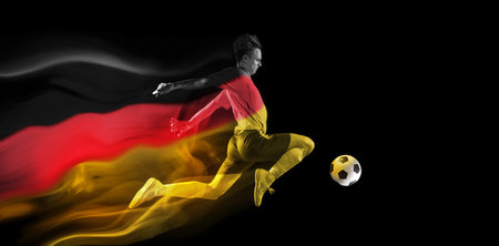 Concentrated young man, soccer athlete training, playing football on black background with flag of Germany elementの写真素材