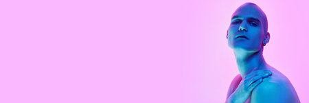 Handsome young man with bald head, shaved face posing shirtless with serious expression on gradient blue pink background in neon lightの写真素材