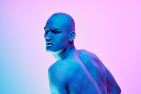 Relief back, Young bald man posing shirtless on gradient blue pink background in neon light. Muscular bodyの写真素材