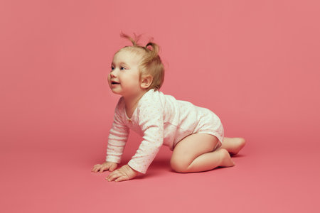 Smiling happy little baby girl, toddler in comfortable  crawling, playing on pink background. Joyful timeの写真素材