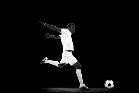 Creative image of young man in white uniform, football player in motion with ball on black background, Monochromeの写真素材