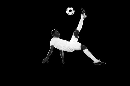 Dynamic image of motivated male soccer playing in motion, training, hitting ball and falling down on lack background. Monochromeの写真素材